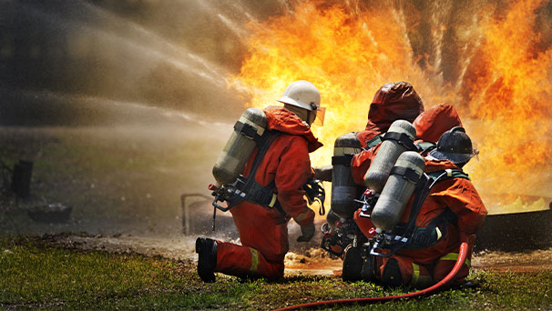 four fireman crouching in front of a fire using a fire hose to put out the fire